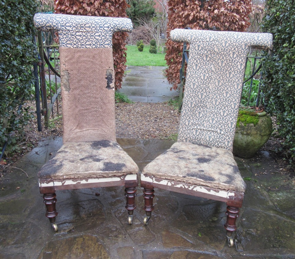 A pair of early Victorian rosewood prie-dieu chairs featuring tall T-bar backs, turned front legs on brass castors, and worn patterned upholstery. View II