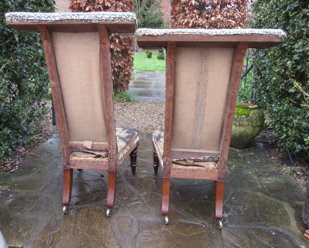 A pair of early Victorian rosewood prie-dieu chairs featuring tall T-bar backs, turned front legs on brass castors, and worn patterned upholstery. View IV