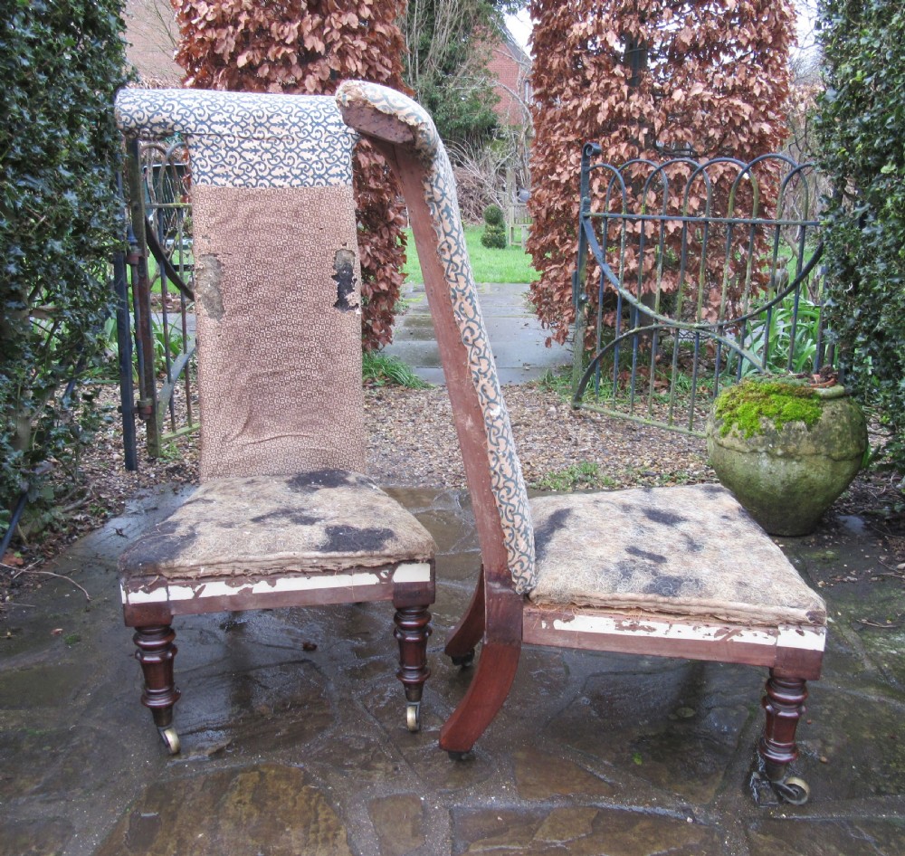 A pair of early Victorian rosewood prie-dieu chairs featuring tall T-bar backs, turned front legs on brass castors, and worn patterned upholstery. View V