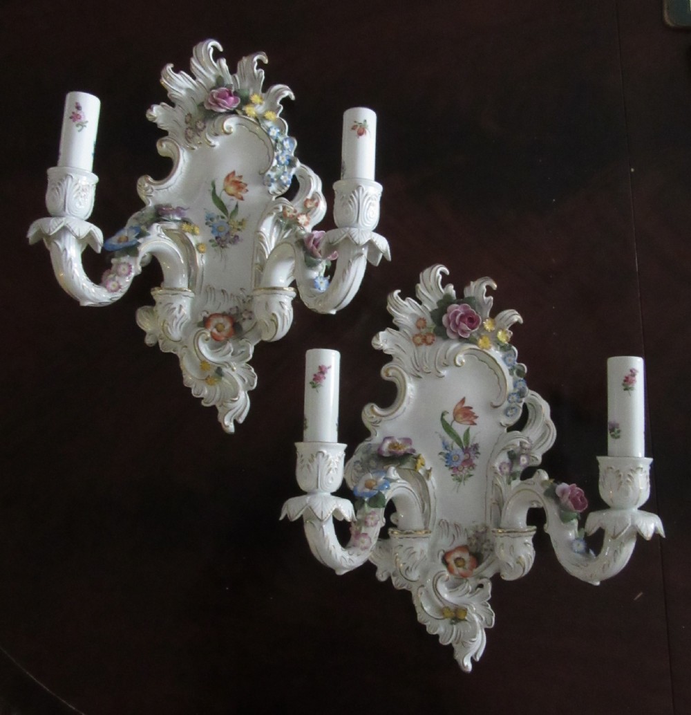 A pair of German Rococo Revival porcelain two-arm wall sconces featuring encrusted polychrome flowers, gilded scrollwork, and hand-painted floral motifs.