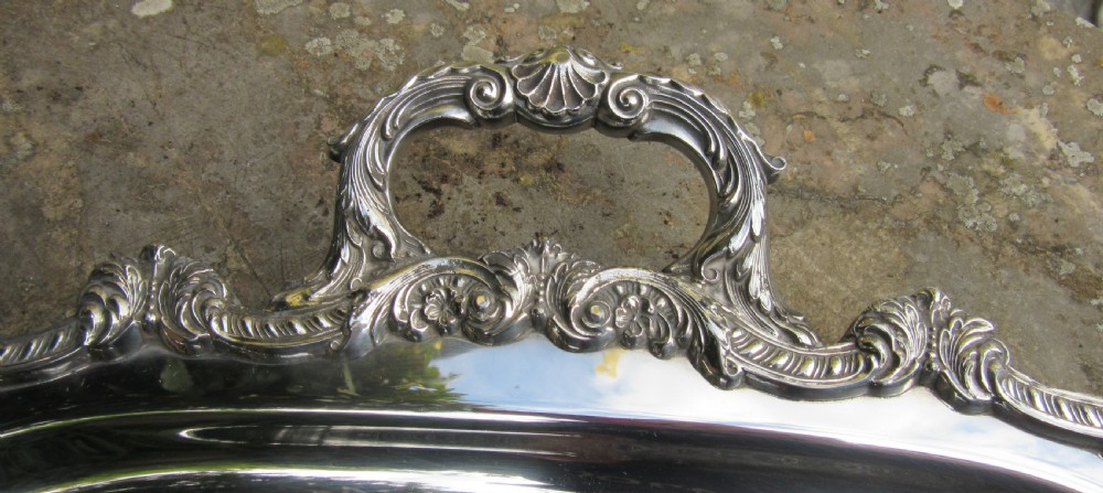 A rectangular Victorian silver-plated tray featuring engraved foliate scrollwork, a shell motif border, and twin cast handles. View VI