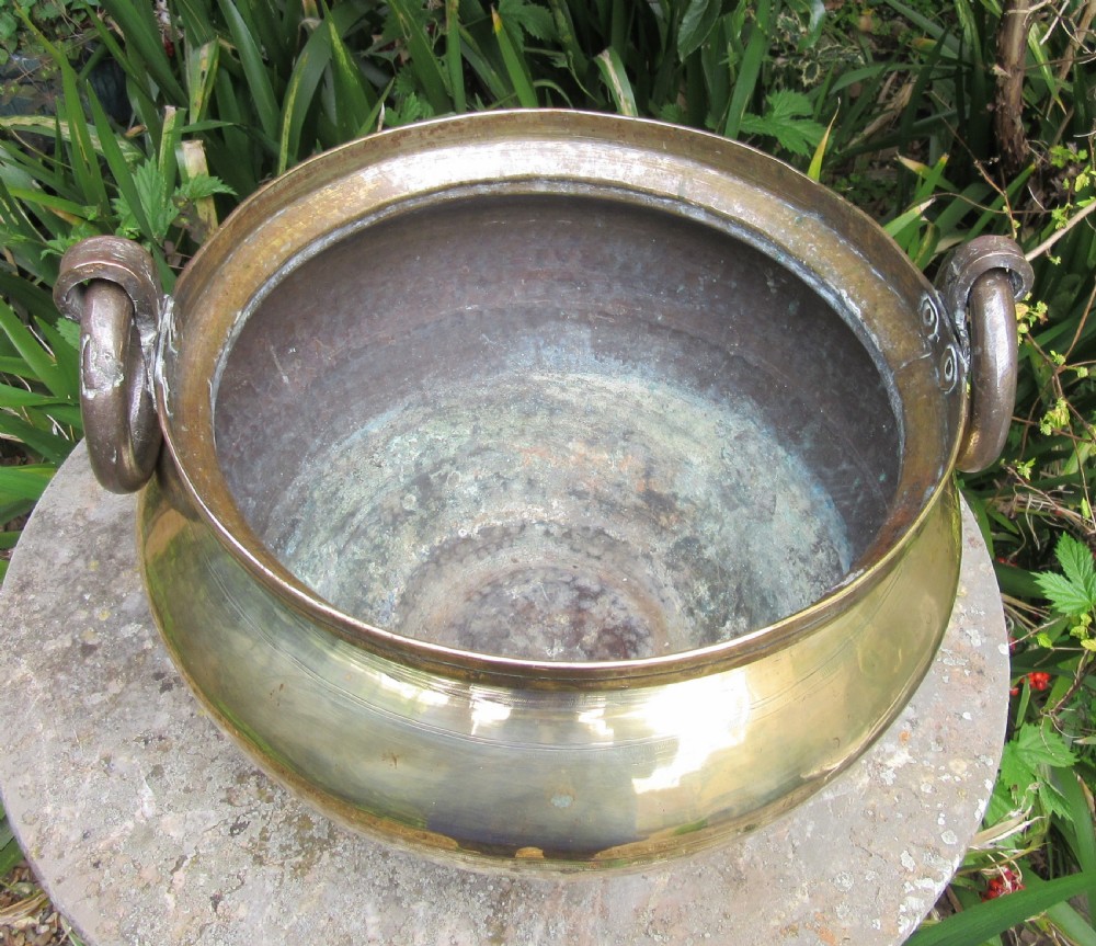 A large antique brass jardiniere featuring a rounded bulbous body, horizontal ribbed details, and two thick ring handles attached to the rolled rim. View III