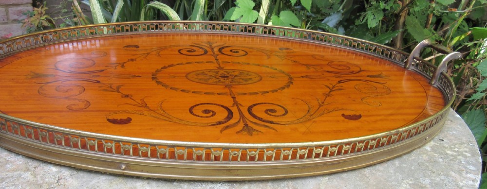 An oval satinwood serving tray featuring detailed central floral marquetry inlay, a pierced brass gallery rim, and two brass handles. View IV