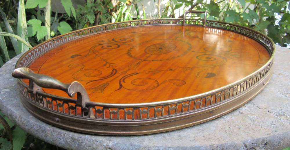 An oval satinwood serving tray featuring detailed central floral marquetry inlay, a pierced brass gallery rim, and two brass handles. View V