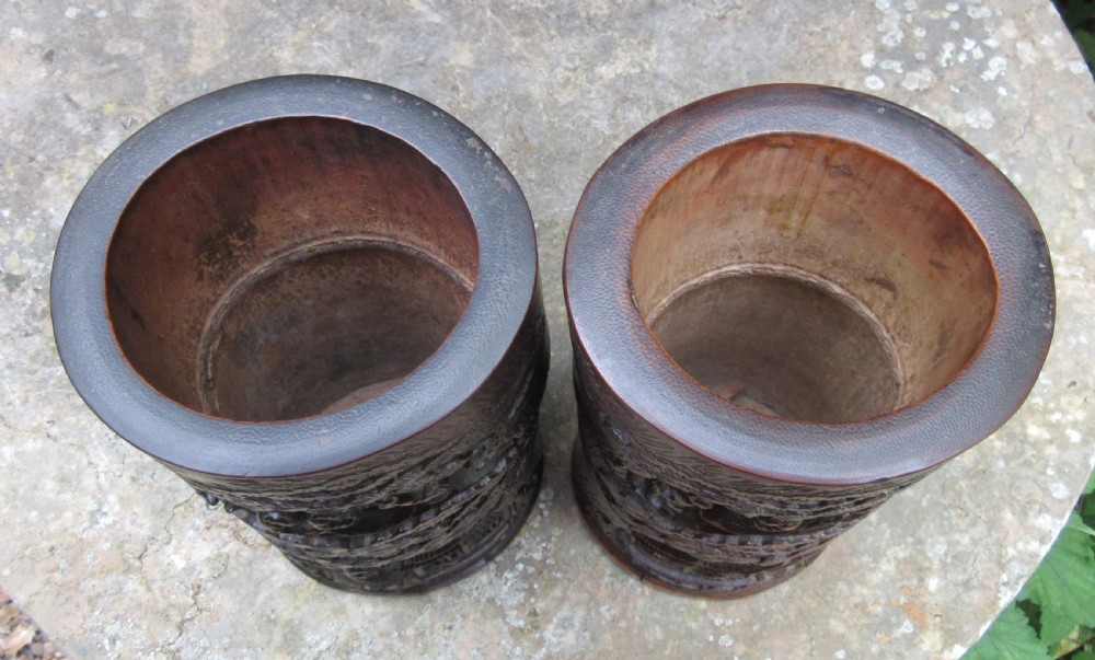 A pair of cylindrical reddish-brown carved bamboo brush pots featuring deep relief carvings of figures, pine trees, and pavilions. View II