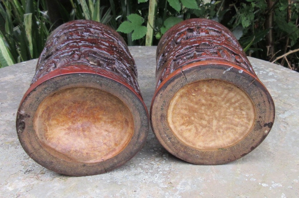 A pair of cylindrical reddish-brown carved bamboo brush pots featuring deep relief carvings of figures, pine trees, and pavilions. View III