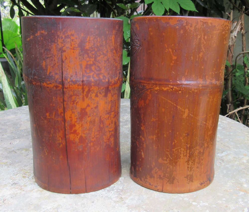A pair of cylindrical reddish-brown carved bamboo brush pots featuring deep relief carvings of figures, pine trees, and pavilions. View V