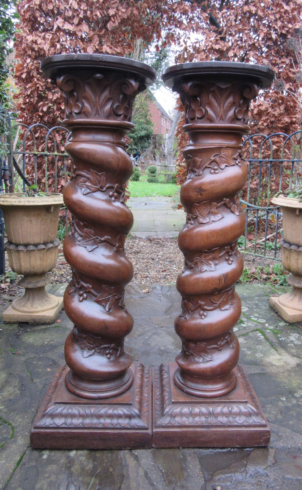 A pair of carved oak spiral column pedestals featuring acanthus leaf capitals, foliage relief carving, and square stepped plinth bases. View V