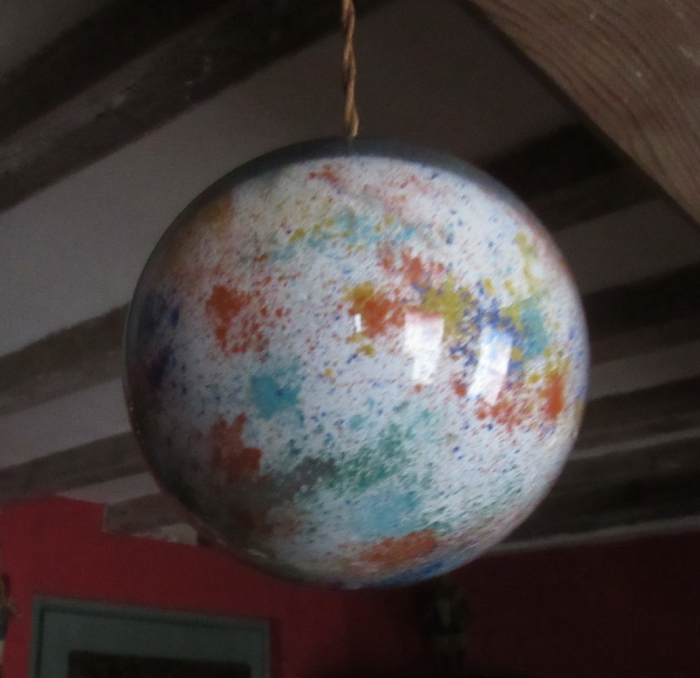 A spherical Victorian potichomania glass witch ball featuring a white base with multicoloured speckled patterns of orange, blue, and yellow.