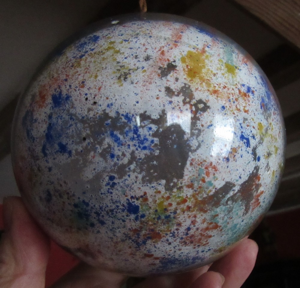 A spherical Victorian potichomania glass witch ball featuring a white base with multicoloured speckled patterns of orange, blue, and yellow. View II