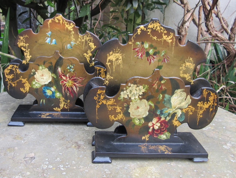 A pair of Regency black papier-mache letter stands decorated with hand-painted floral motifs and gilded foliage on stepped rectangular bases.