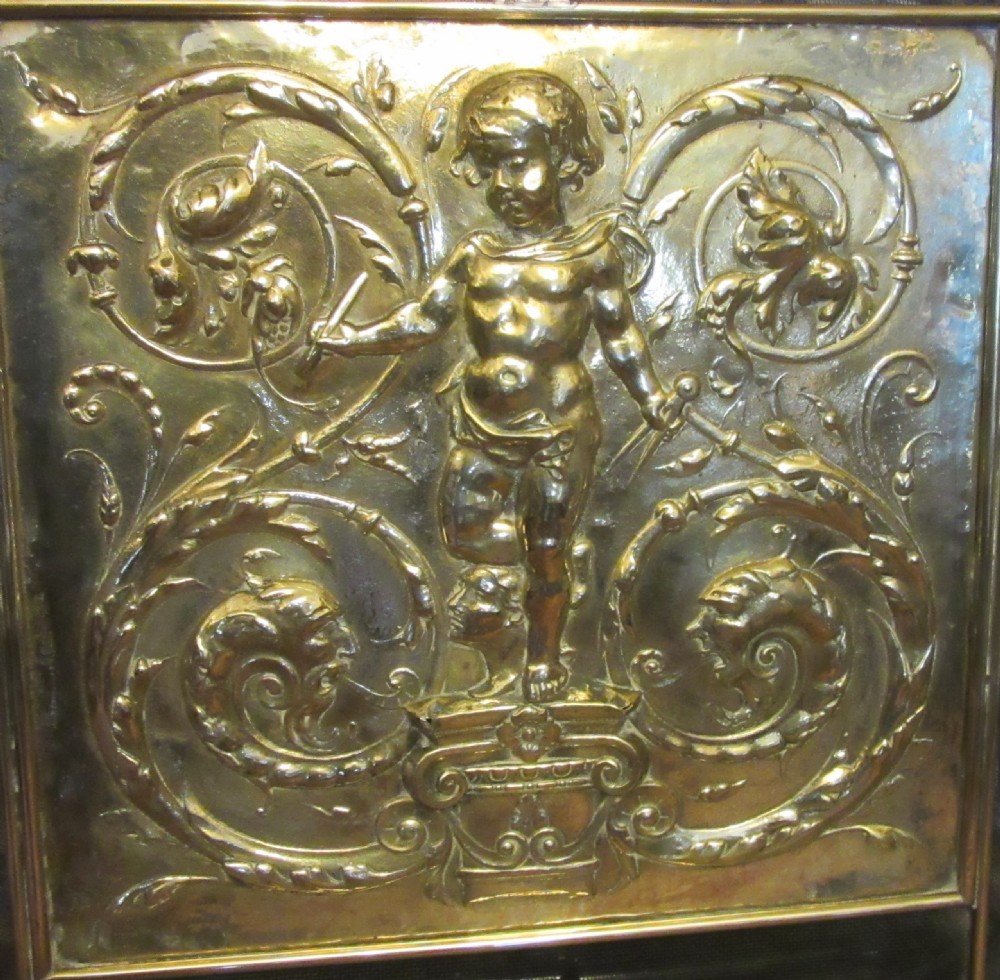 An antique embossed brass fire screen featuring a central panel with a cherub motif framed by wire mesh. View III