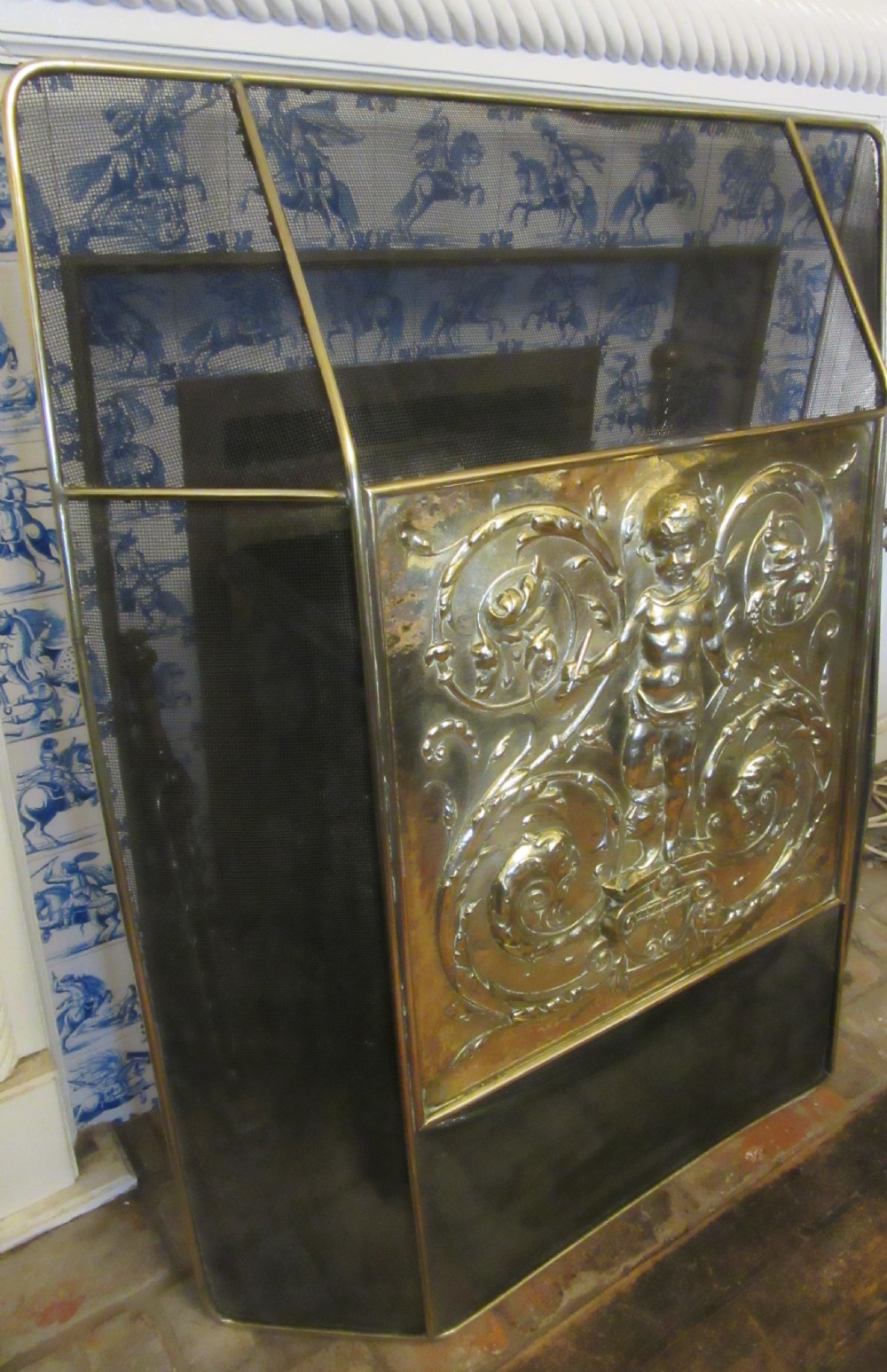 An antique embossed brass fire screen featuring a central panel with a cherub motif framed by wire mesh. View IV