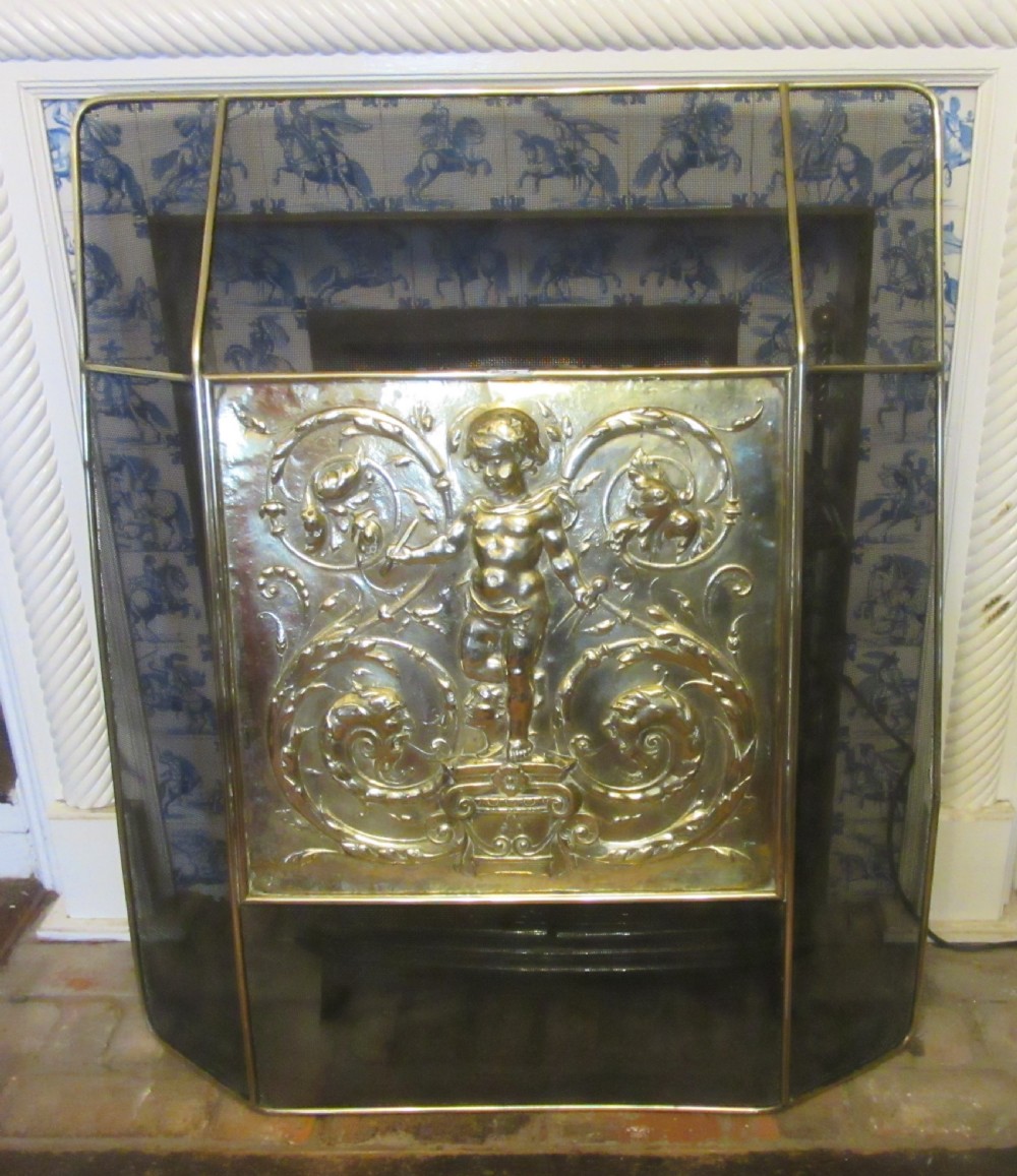 An antique embossed brass fire screen featuring a central panel with a cherub motif framed by wire mesh. View V