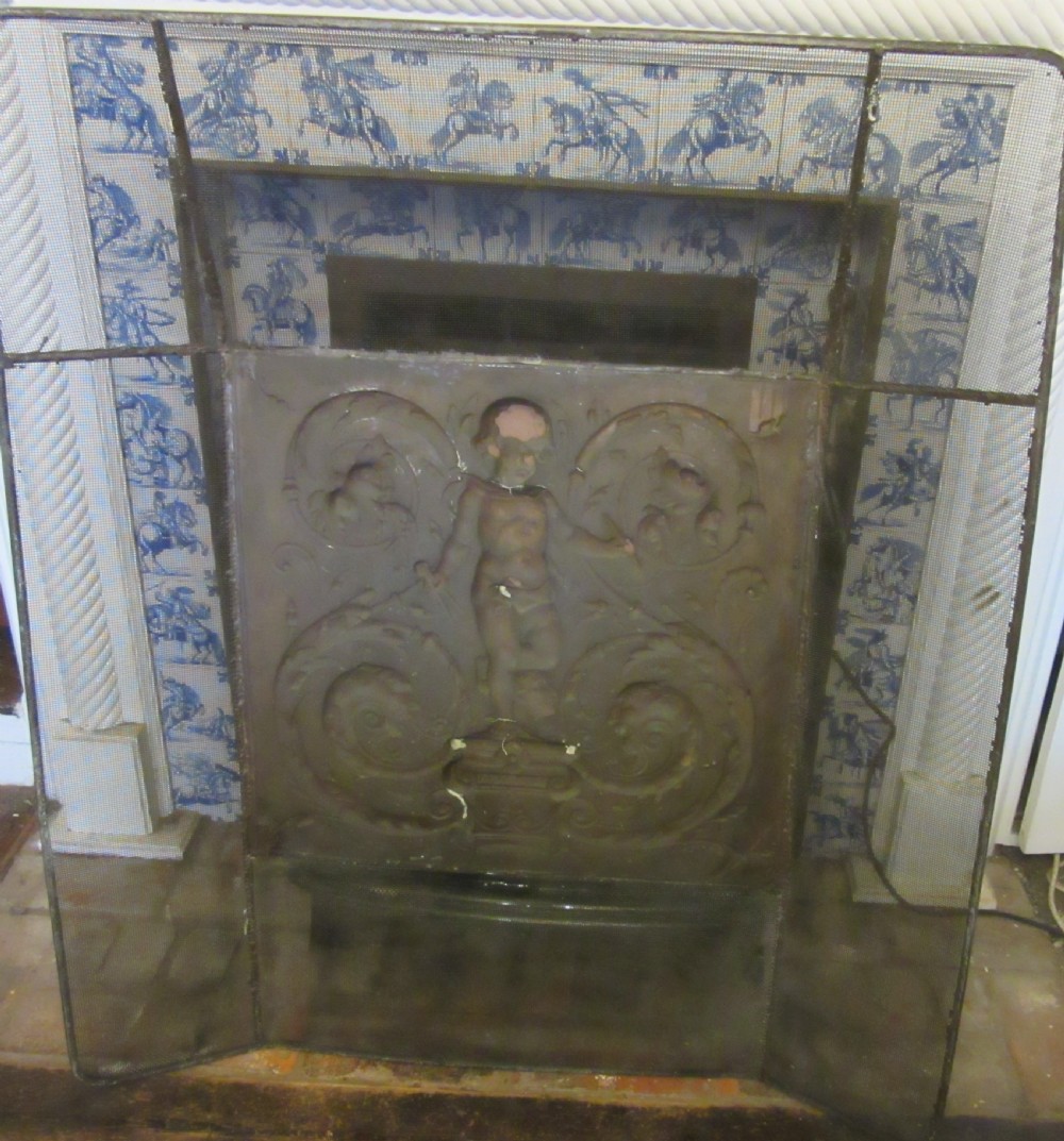 An antique embossed brass fire screen featuring a central panel with a cherub motif framed by wire mesh. View VII