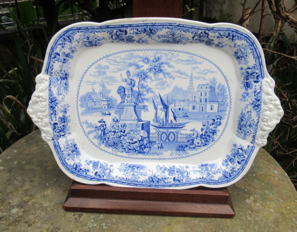 A rectangular blue and white transferware platter decorated with classical statues, buildings, and a sailboat scene with molded side handles.