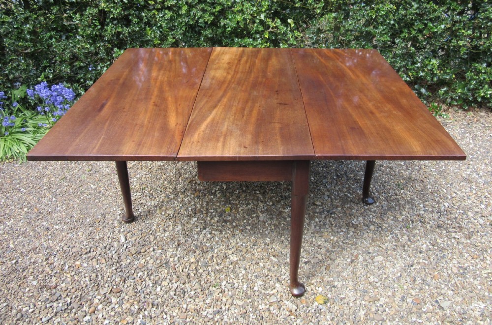A Georgian mahogany drop-leaf dining table shown with extended leaves and tapered legs ending in pad feet.