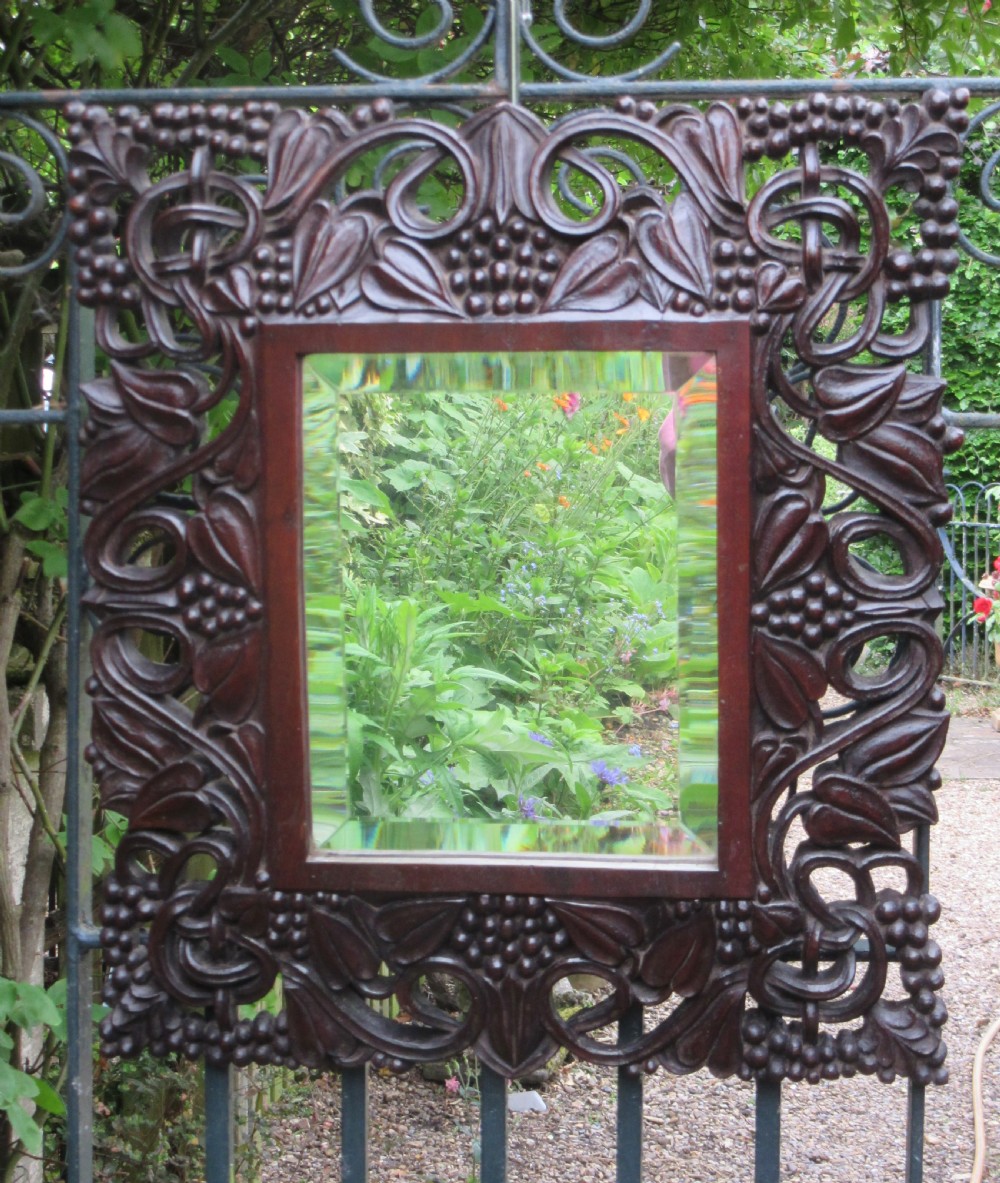 A square dark hardwood Anglo-Indian wall mirror featuring intricate pierced openwork floral and foliate hand carving surrounding a bevelled glass mirror plate. View II