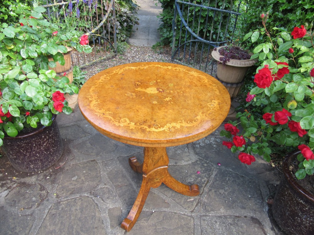 An early Victorian burr walnut tripod side table featuring a circular top, a tapered stem with inlaid floral motifs, and three splayed legs with scrolled feet. View V