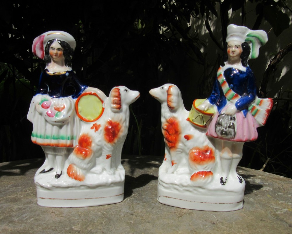 A pair of Victorian Staffordshire glazed earthenware figures depicting a male and female musician dressed in traditional attire, each accompanied by a white and orange spaniel.