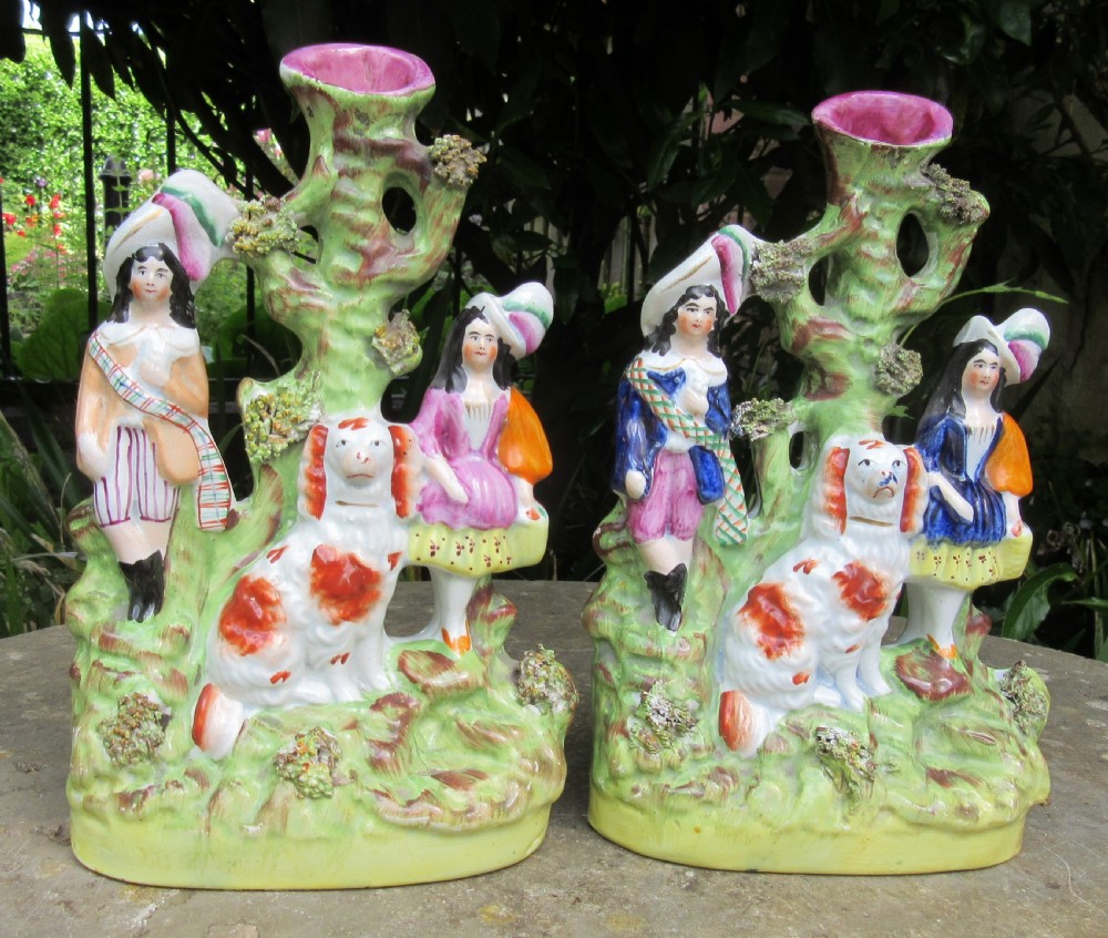 A pair of 19th-century Victorian Staffordshire earthenware spill vases featuring hand-painted figures, spaniels, and hollow tree trunk forms.