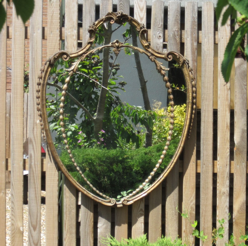 A 19th-century shield-shaped wall mirror featuring a gilded frame with carved scrollwork cresting, leaf motifs, and beadwork border. View V