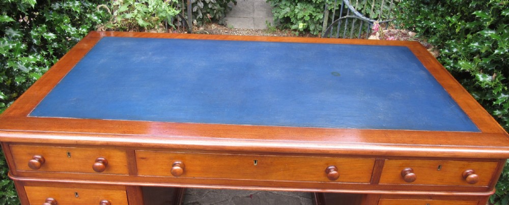 A nineteenth-century Victorian mahogany pedestal desk featuring a blue leather writing surface, multiple drawers with wooden turned handles, and twin pedestal supports. View III