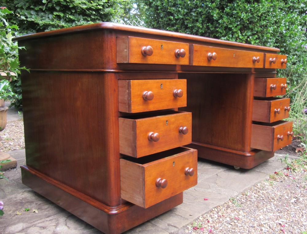 A nineteenth-century Victorian mahogany pedestal desk featuring a blue leather writing surface, multiple drawers with wooden turned handles, and twin pedestal supports. View IV
