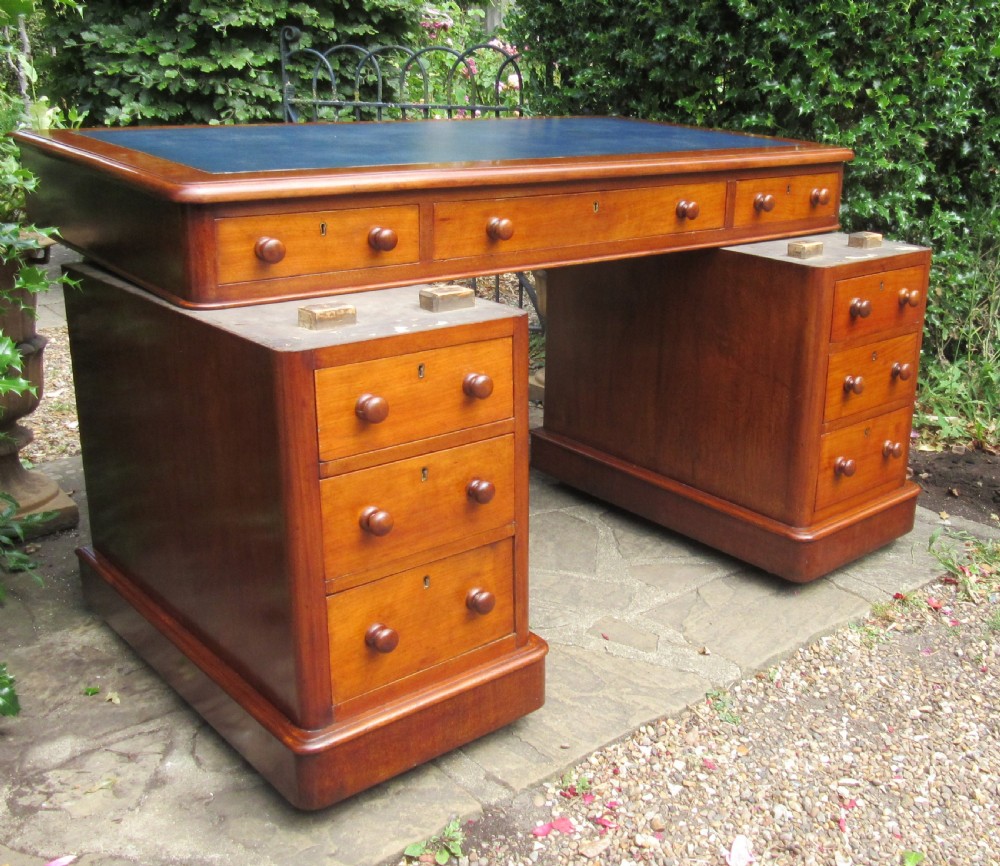 A nineteenth-century Victorian mahogany pedestal desk featuring a blue leather writing surface, multiple drawers with wooden turned handles, and twin pedestal supports. View V