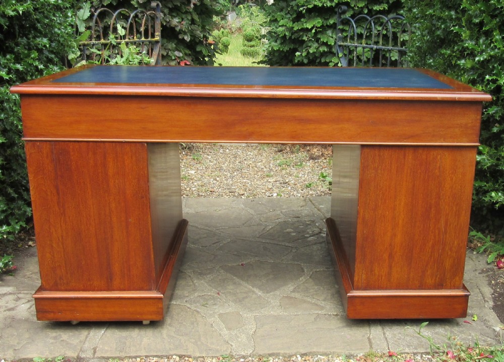 A nineteenth-century Victorian mahogany pedestal desk featuring a blue leather writing surface, multiple drawers with wooden turned handles, and twin pedestal supports. View VI