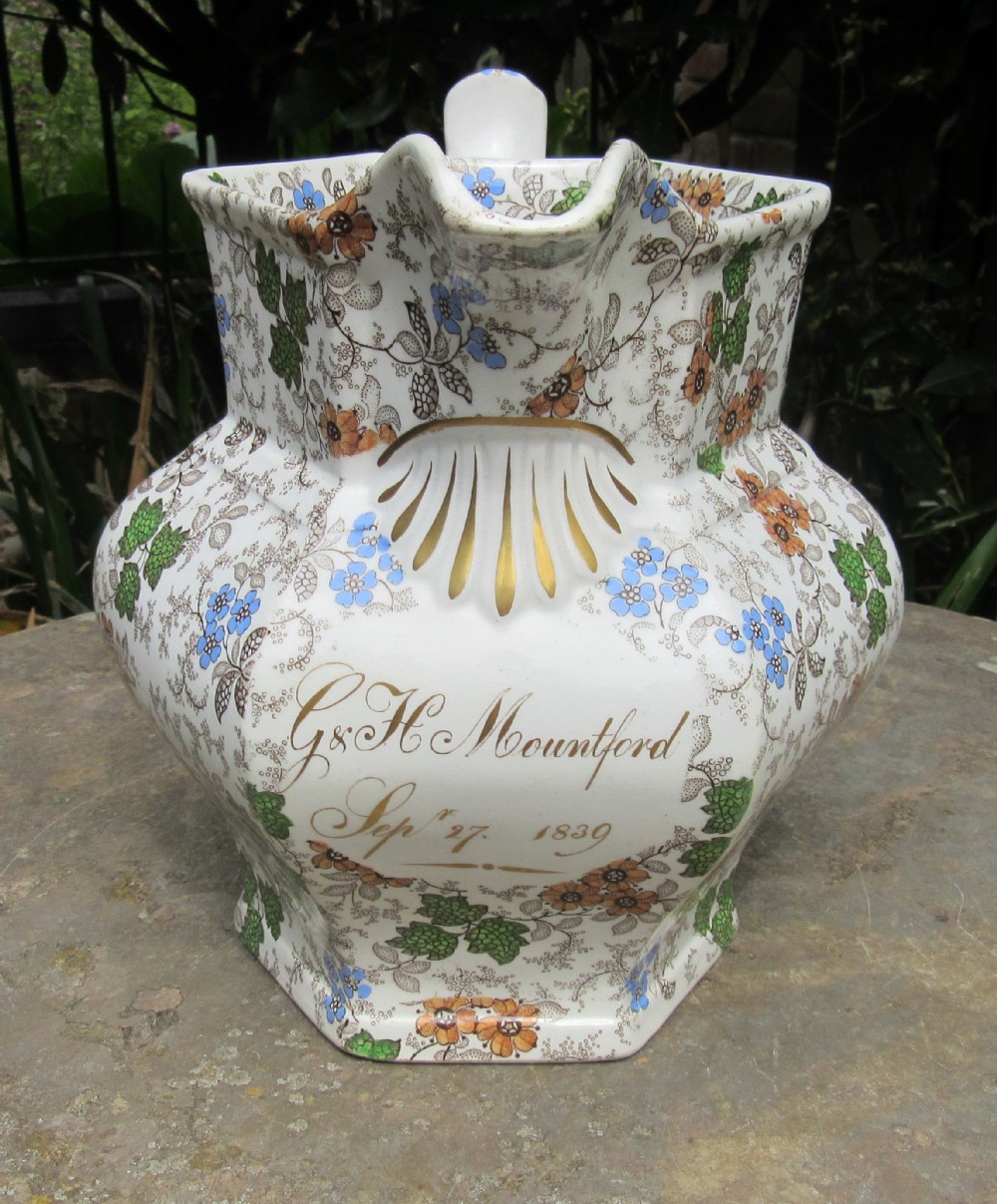 An octagonal white ceramic jug with colourful floral transferware, a moulded gilt shell detail, and handwritten gold lettering dated September 27 1839.