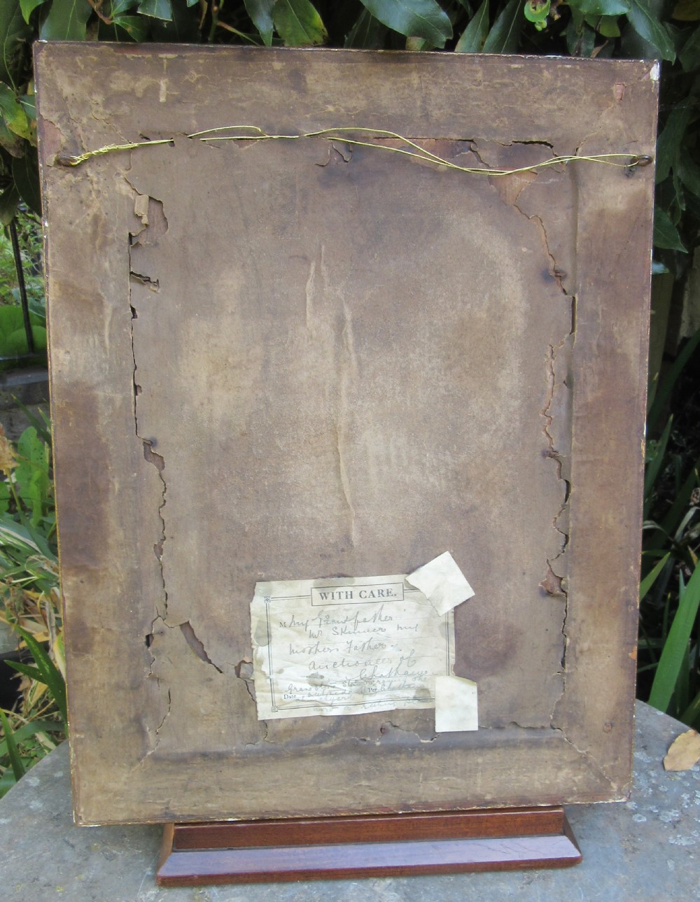 An antique primitive watercolour portrait painting depicting a seated gentleman in a garden setting within a detailed moulded frame. View IV