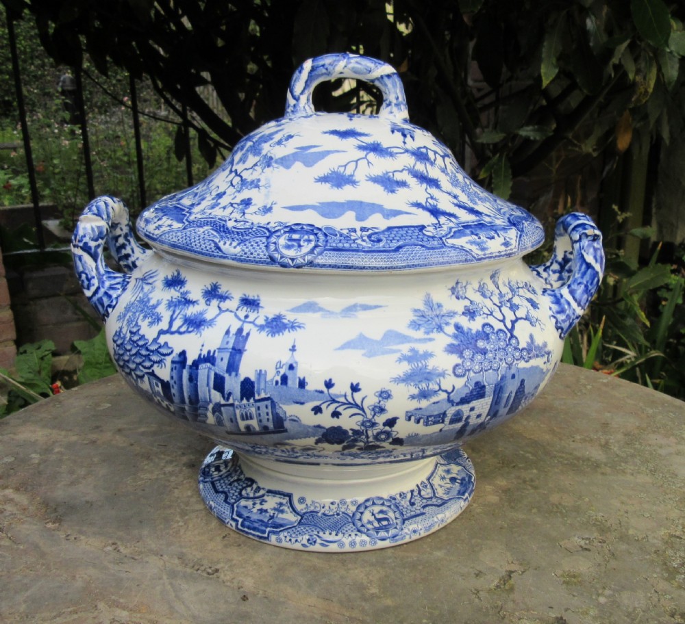 A blue and white transfer-printed ceramic tureen featuring a domed lid, side handles, and a pedestal base decorated with landscape scenes.