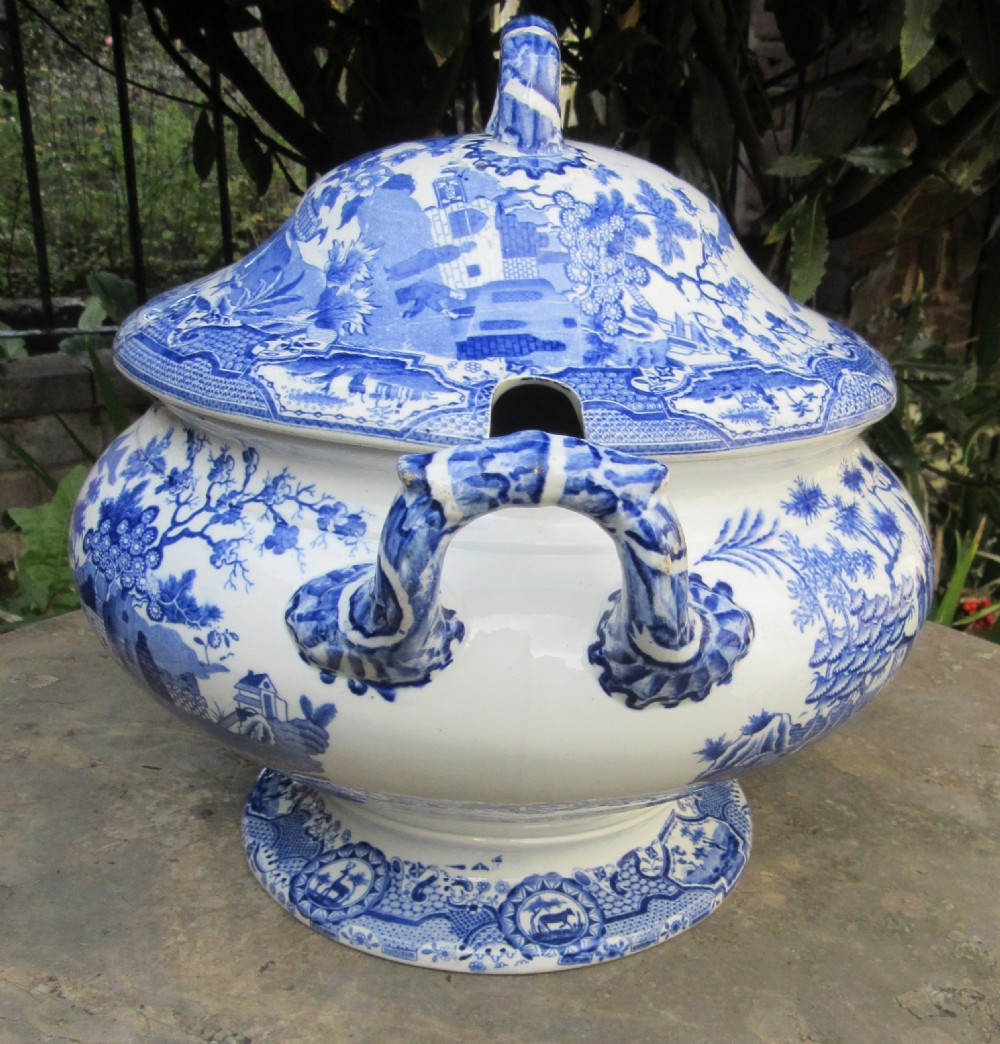 A blue and white transfer-printed ceramic tureen featuring a domed lid, side handles, and a pedestal base decorated with landscape scenes. View II