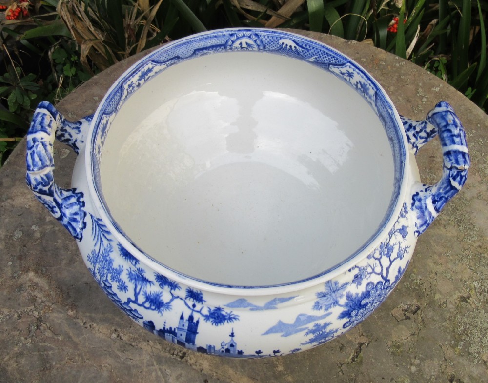 A blue and white transfer-printed ceramic tureen featuring a domed lid, side handles, and a pedestal base decorated with landscape scenes. View III