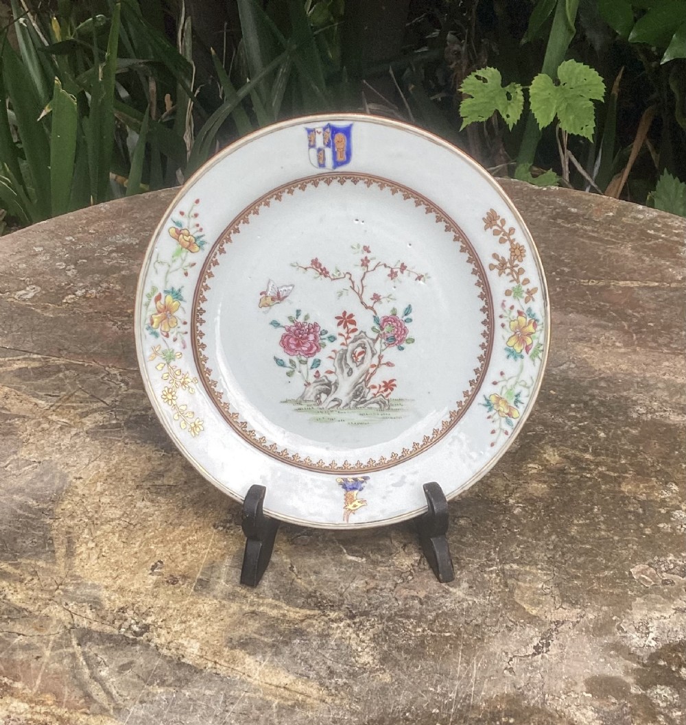 A circular Chinese export porcelain armorial plate featuring a hand-painted coat of arms at the top rim and a central botanical scene.