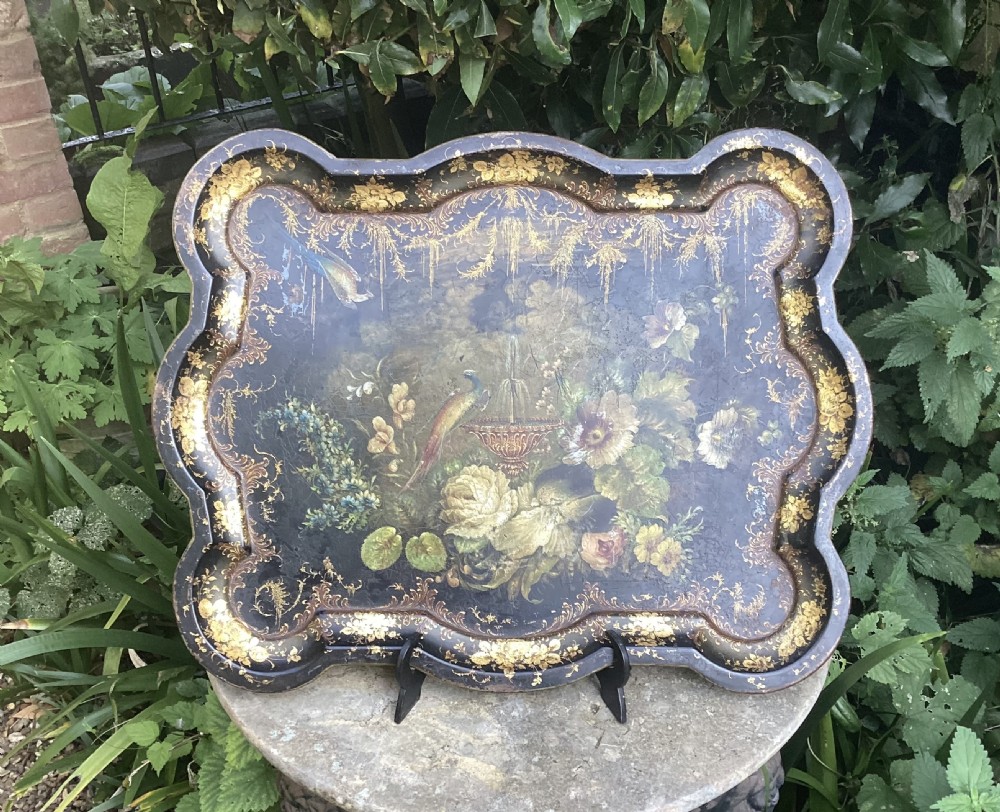 A dark shaped Regency toleware tray featuring hand-painted botanical flowers, a bird, and elaborate gilded border embellishments.