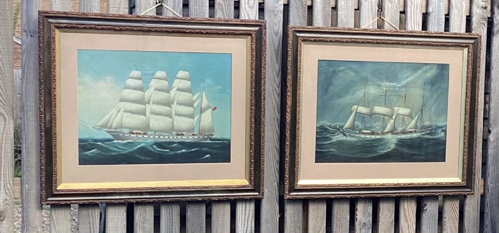 A pair of framed early 20th-century maritime oil paintings depicting a three-masted barque sailing ship at sea in contrasting weather conditions.