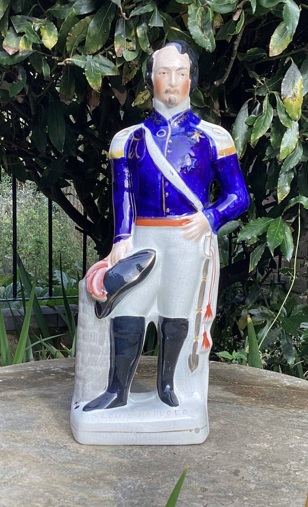 A Victorian Staffordshire earthenware figure depicting Louis Napoleon standing in a cobalt blue military tunic, white trousers, and black riding boots.