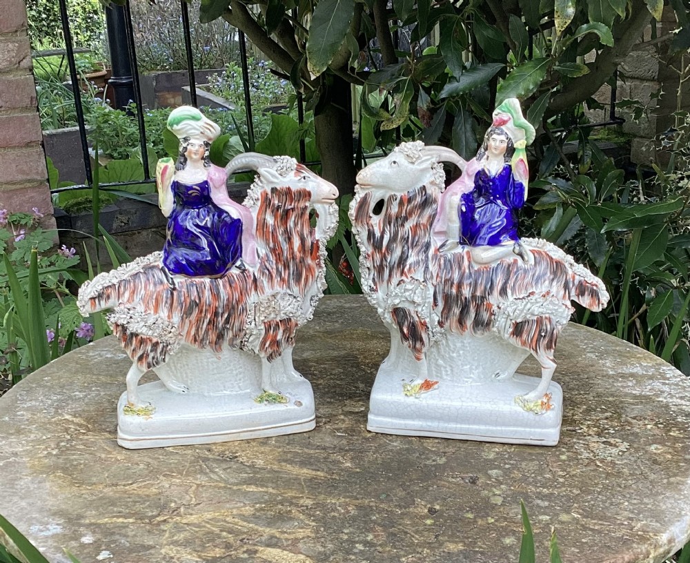 A pair of Victorian Staffordshire earthenware figures showing figures seated on long-haired goats with hand-painted enamel decoration.