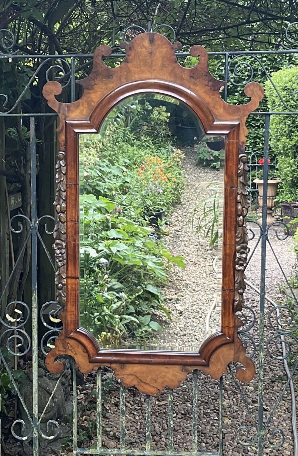 A Georgian style walnut wall mirror featuring a fret-cut scrollwork cresting, carved side foliage, and a bevelled glass mirror plate.