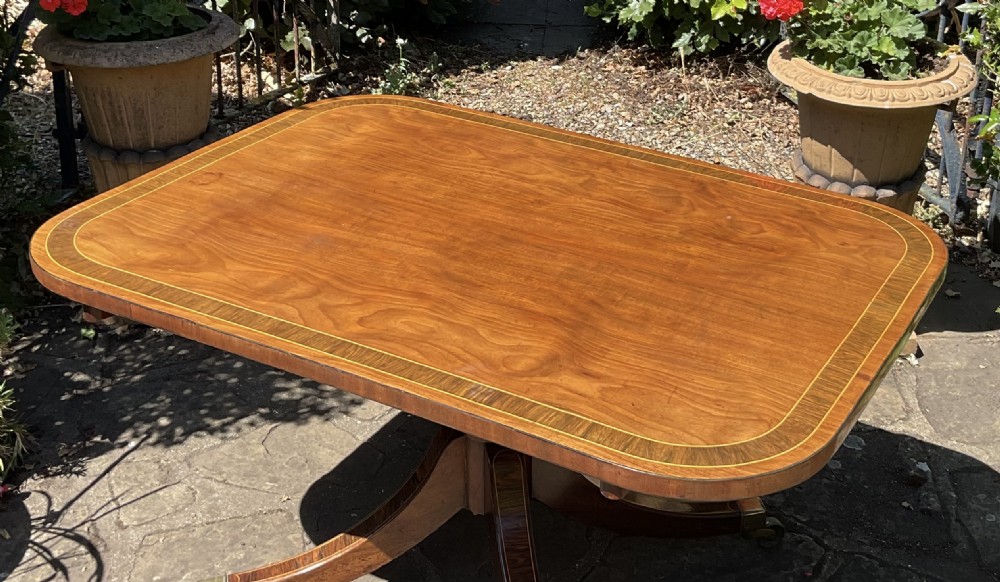 A Regency mahogany coffee table featuring an inlaid crossbanded top, central turned column, and splayed legs with brass castors. View II