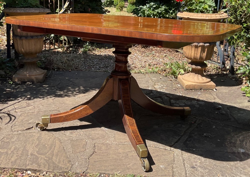 A Regency mahogany coffee table featuring an inlaid crossbanded top, central turned column, and splayed legs with brass castors. View V