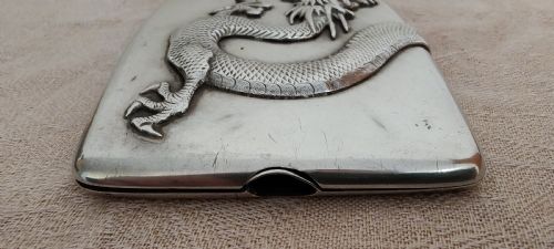 fig 1. A rectangular silver Art Deco cigarette case featuring a detailed raised dragon motif across the front surface.