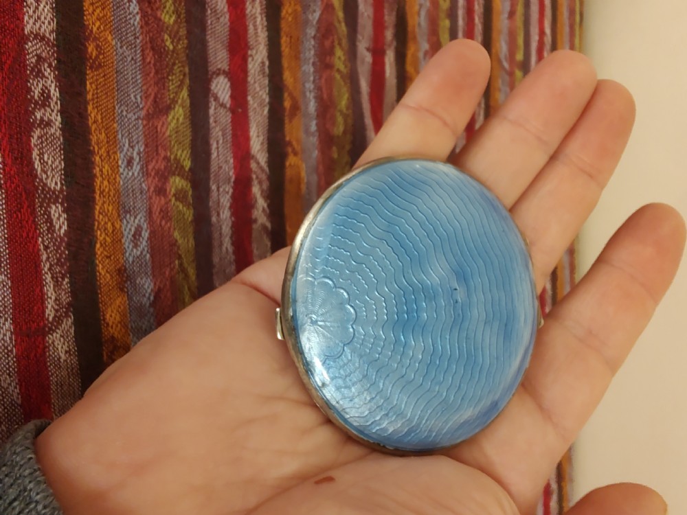 An oval Art Deco solid silver powder compact decorated with light blue guilloche enamel over a wavy engine-turned background.