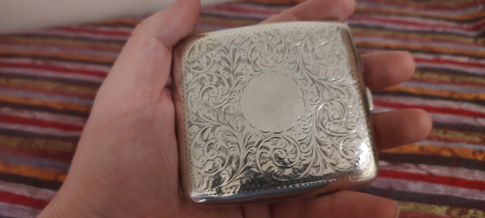 A square Victorian sterling silver cigarette case featuring hand-engraved foliate scrollwork and a blank central scalloped cartouche.