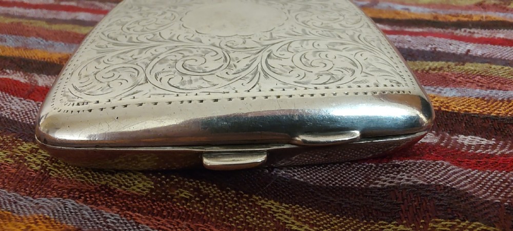 A square Victorian sterling silver cigarette case featuring hand-engraved foliate scrollwork and a blank central scalloped cartouche. View II