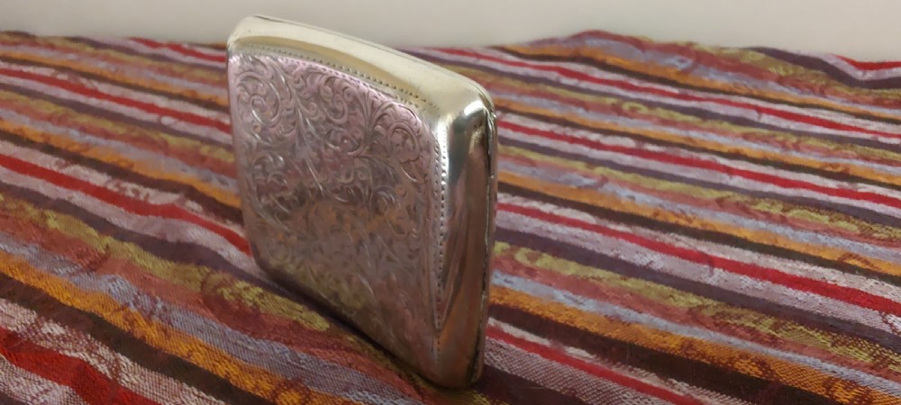 A square Victorian sterling silver cigarette case featuring hand-engraved foliate scrollwork and a blank central scalloped cartouche. View V