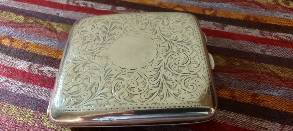 A square Victorian sterling silver cigarette case featuring hand-engraved foliate scrollwork and a blank central scalloped cartouche. View XV
