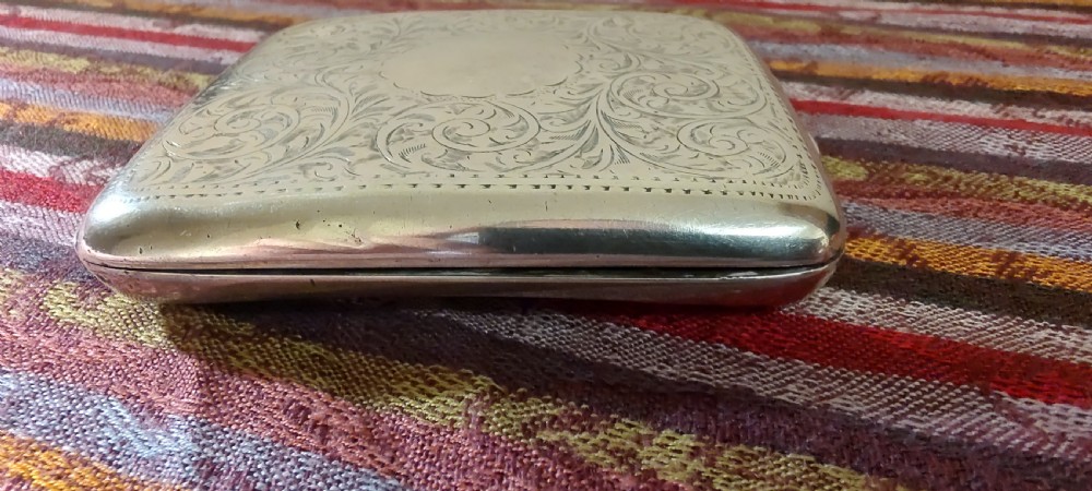A square Victorian sterling silver cigarette case featuring hand-engraved foliate scrollwork and a blank central scalloped cartouche. View XVI